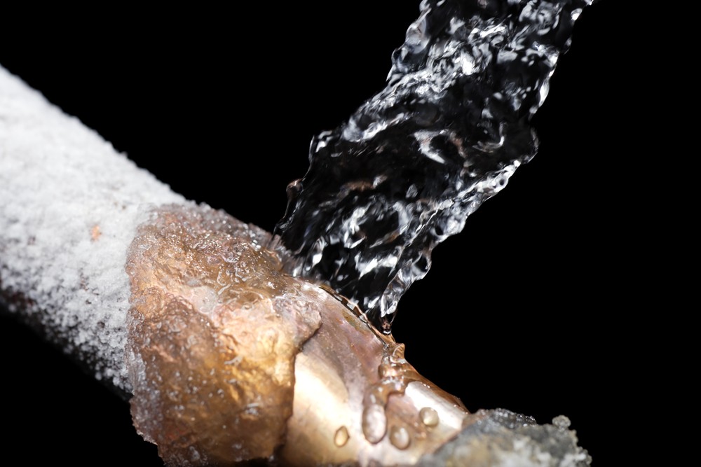Close-up of a frozen pipe with water leaking from a burst section