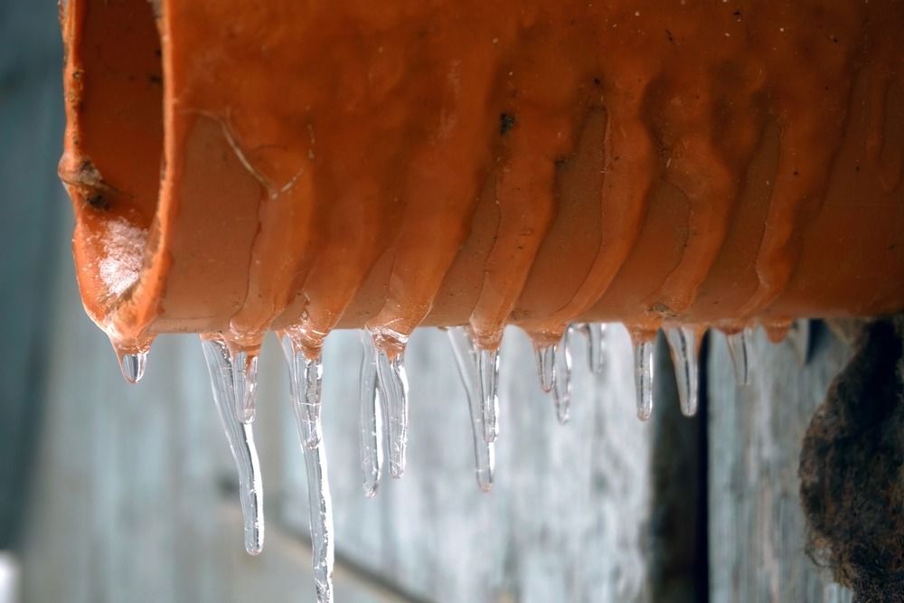 Close-up of icicles hanging from the bottom edge of an orange pipe